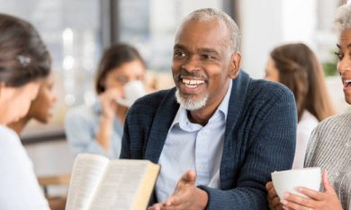 Handsome senior African American man gestures while studying the Bible with his friends in a coffee shop.